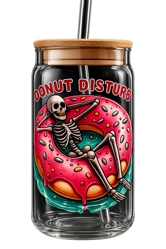 A clear glass tumbler with a bamboo lid and black straw, featuring a colorful graphic of a skeleton lounging inside a pink donut with the text 'DONUT DISTURB' in red outlined letters.